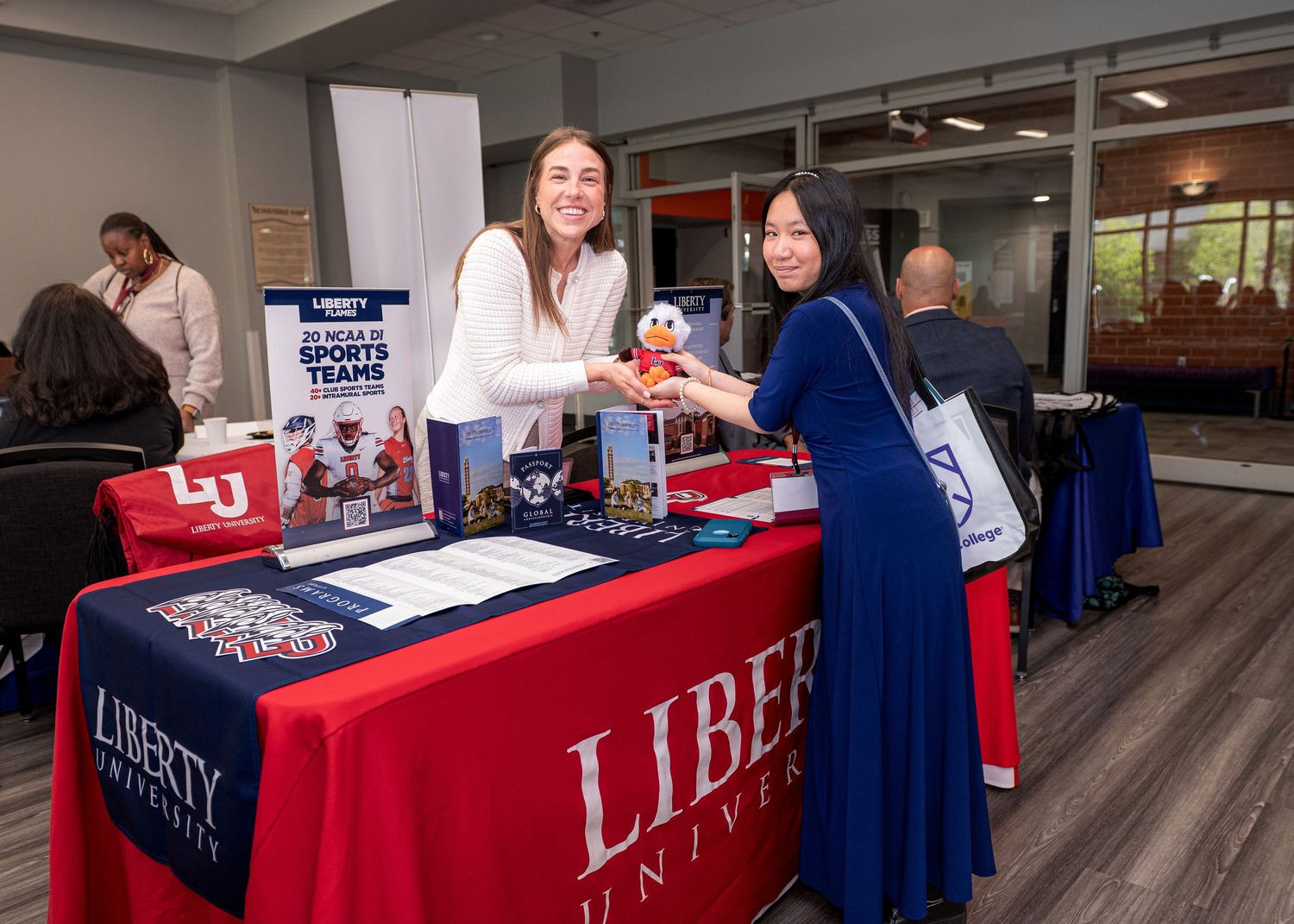 College fair with red-clothed tables displaying Liberty University materials and information.