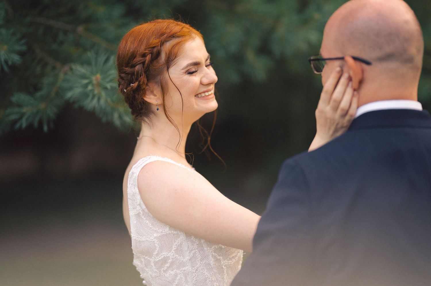 A tender moment between newlyweds sharing an intimate outdoor embrace against an evergreen backdrop.