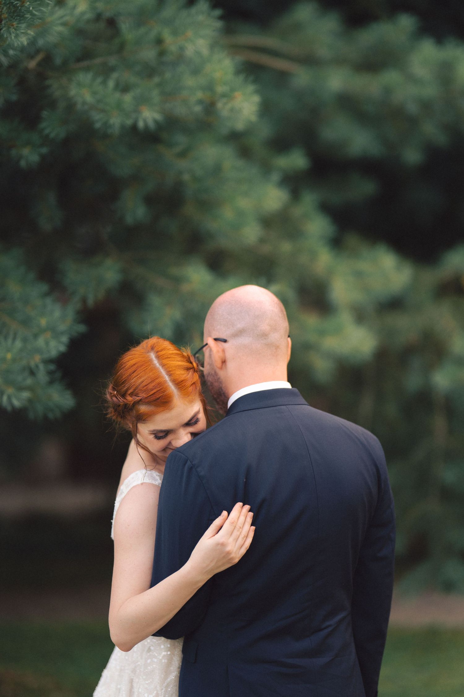 A romantic wedding couple shares an intimate moment outdoors with lush green foliage in the background.