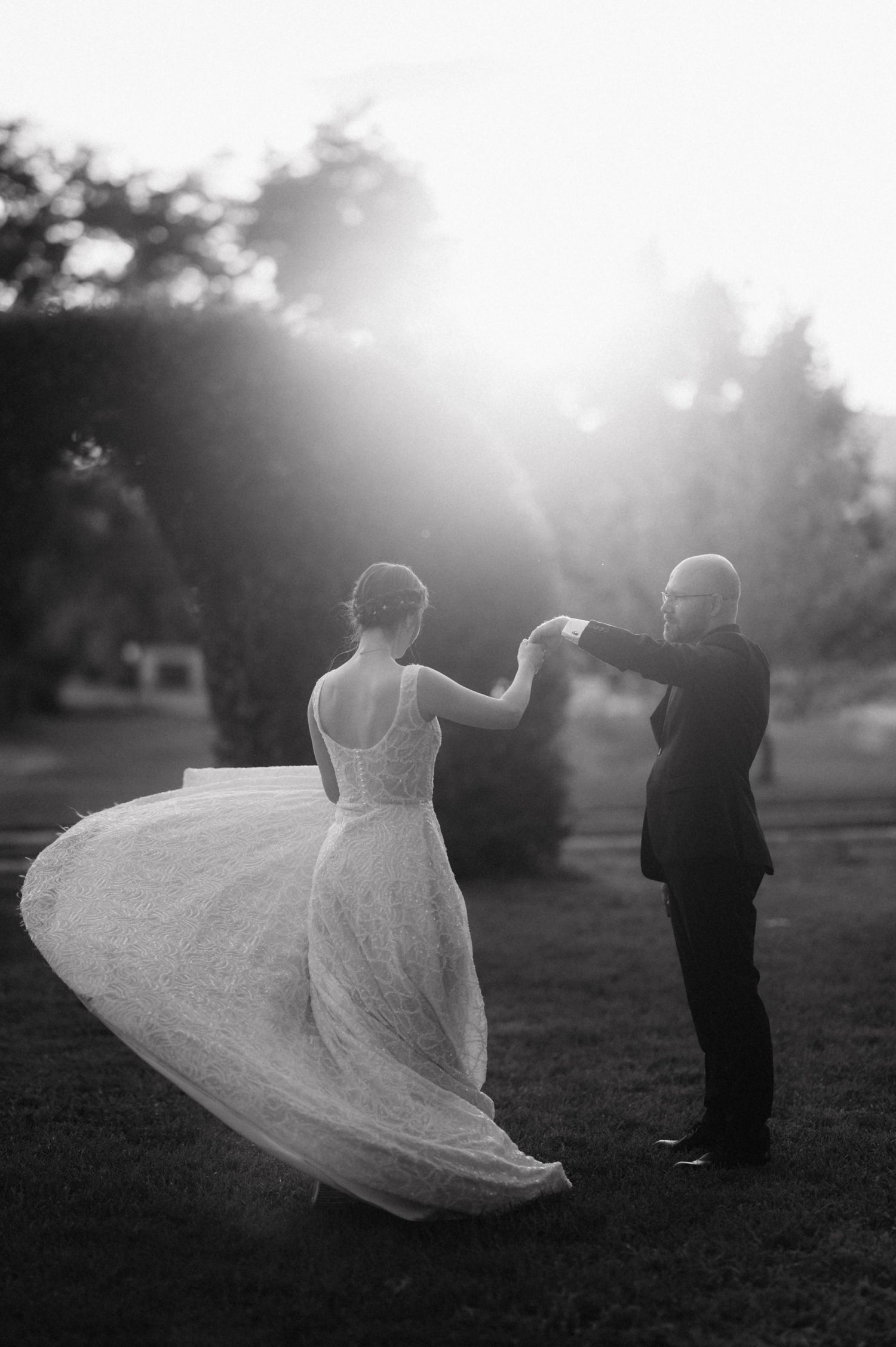 A romantic black and white wedding photo shows a couple dancing outdoors at sunset, with the bride's dress swirling gracefully.