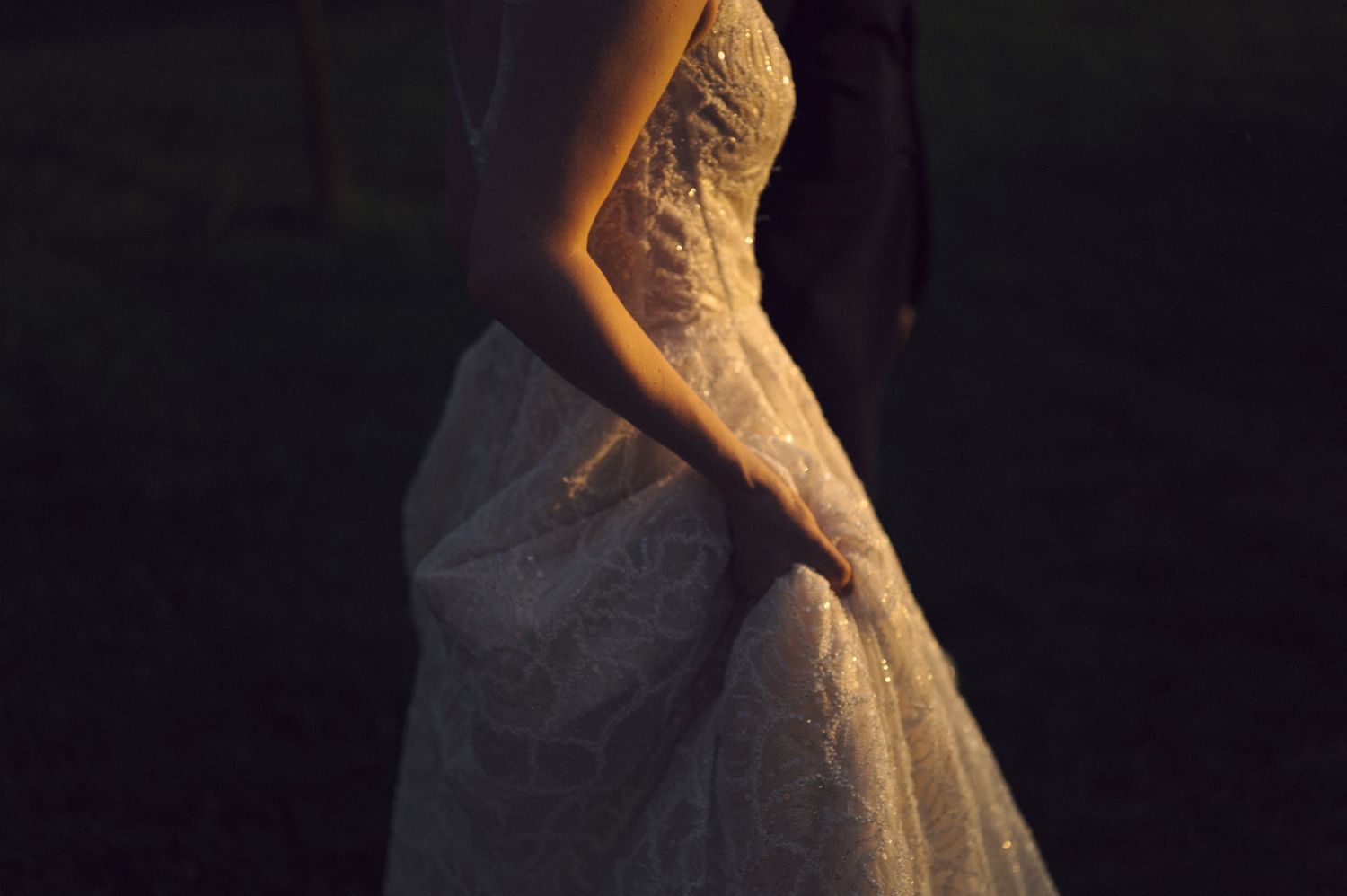 A close-up view of a white lace wedding dress silhouette illuminated against a dark background.