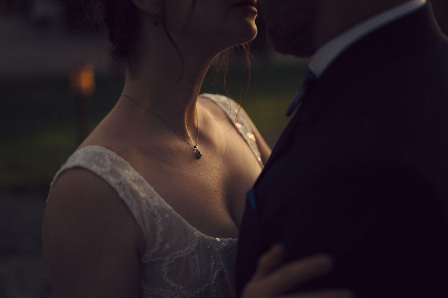A wedding couple shares a tender moment outdoors as the sun sets, creating a romantic silhouette against the sky.