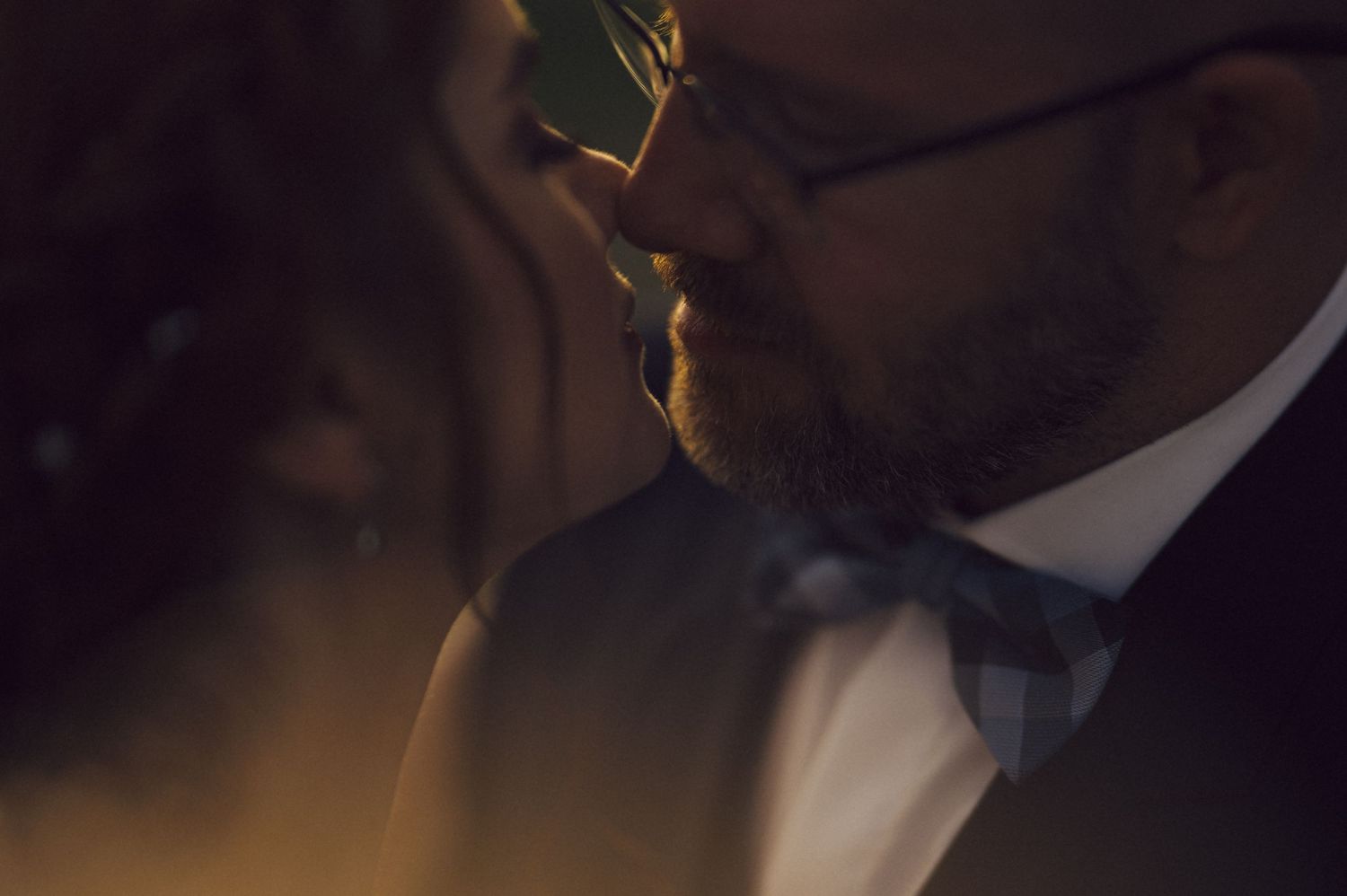 A close up moment of quiet intimacy between a couple in formal evening wear, illuminated by soft golden lighting.