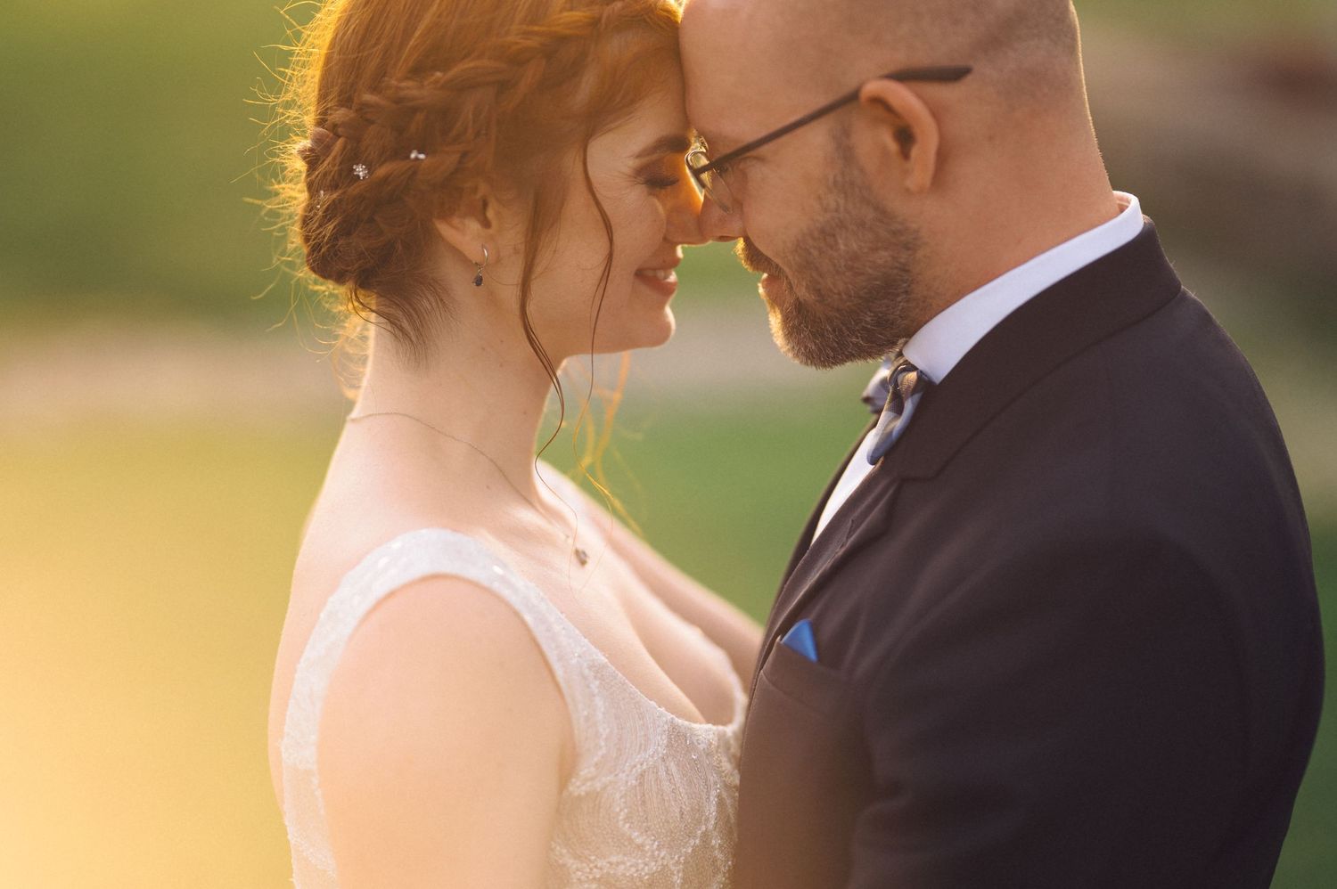 A bride and groom share an intimate moment at sunset, with warm golden light illuminating their formal wedding attire.