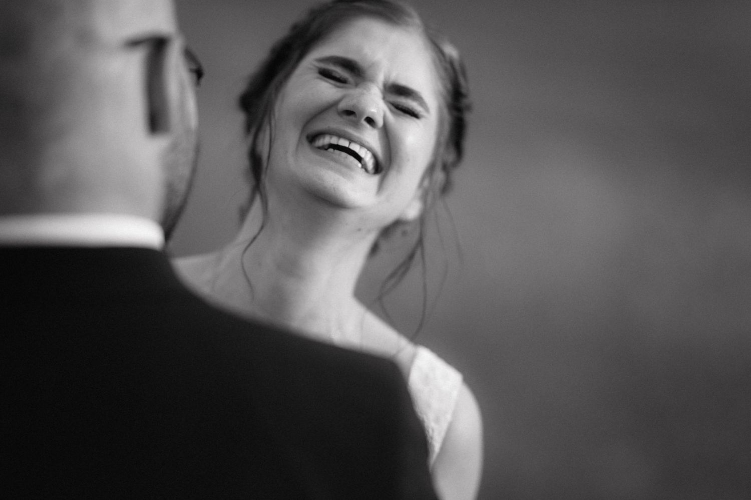 Black and white candid wedding photo showing a bride laughing joyfully during an intimate moment with the groom.