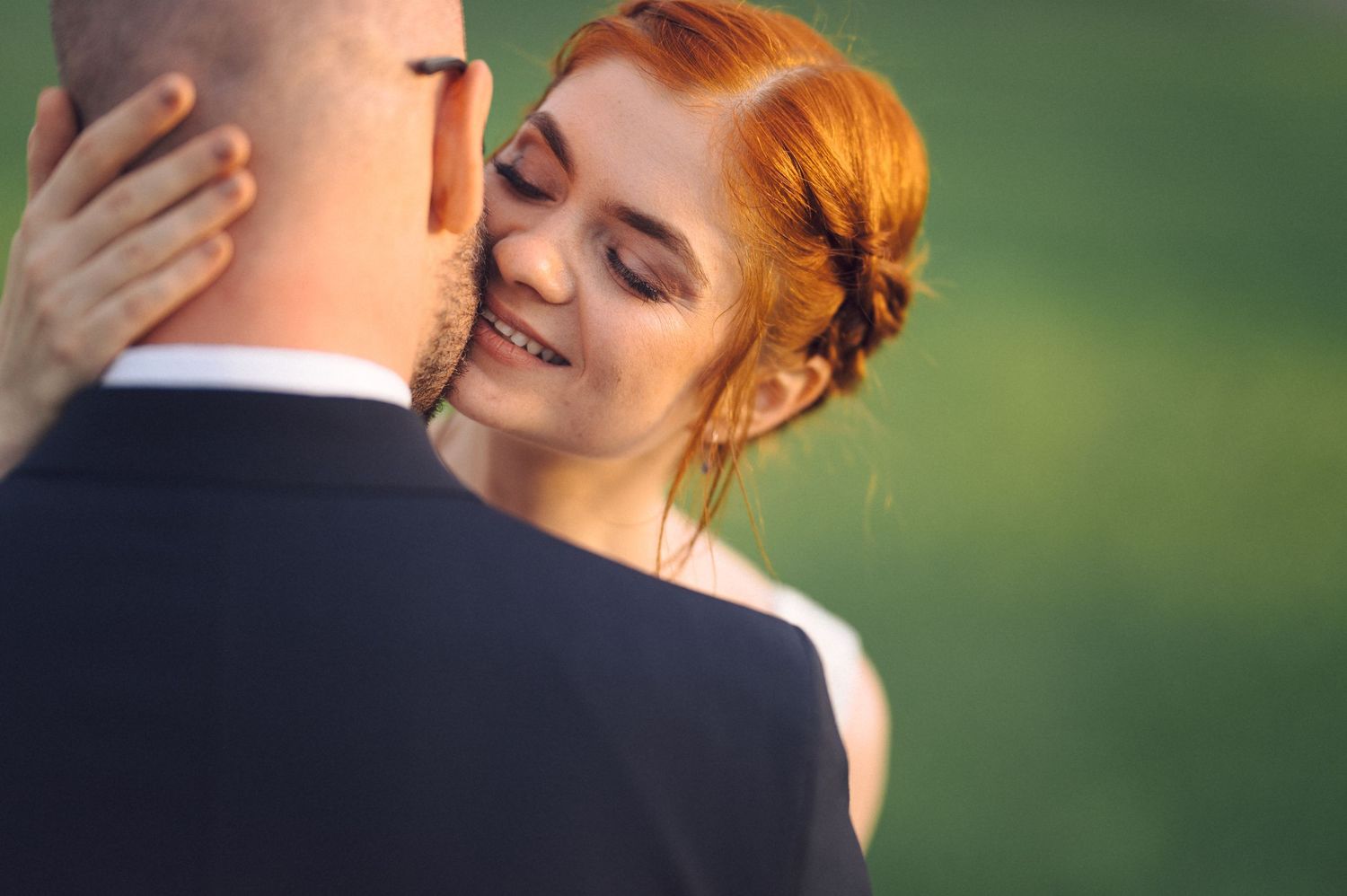 A tender moment between a couple in formalwear against a blurred green background.