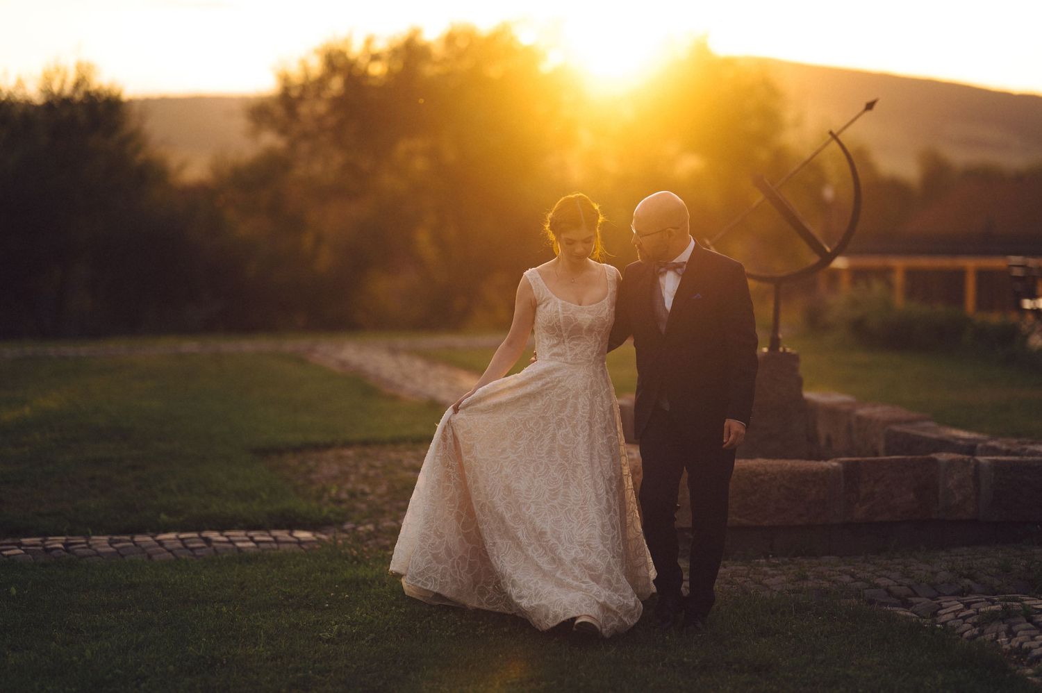A couple stands silhouetted against a golden sunset in a romantic outdoor wedding setting.