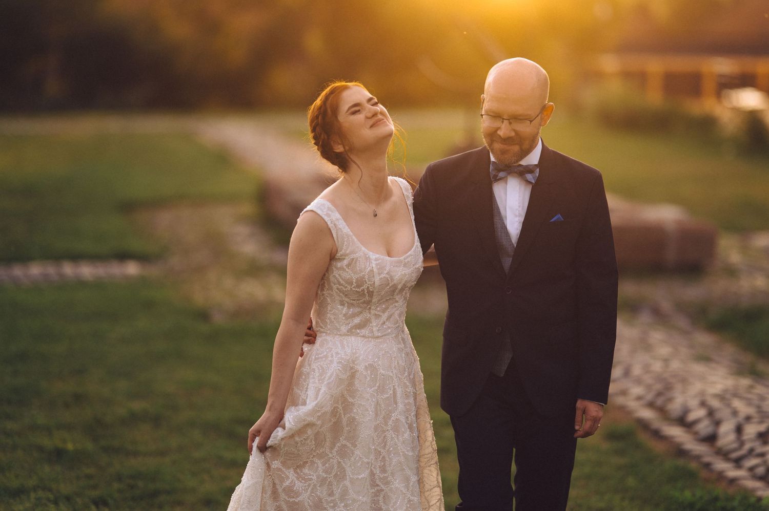 A romantic sunset wedding portrait of a couple in formal attire laughing together in a garden setting.