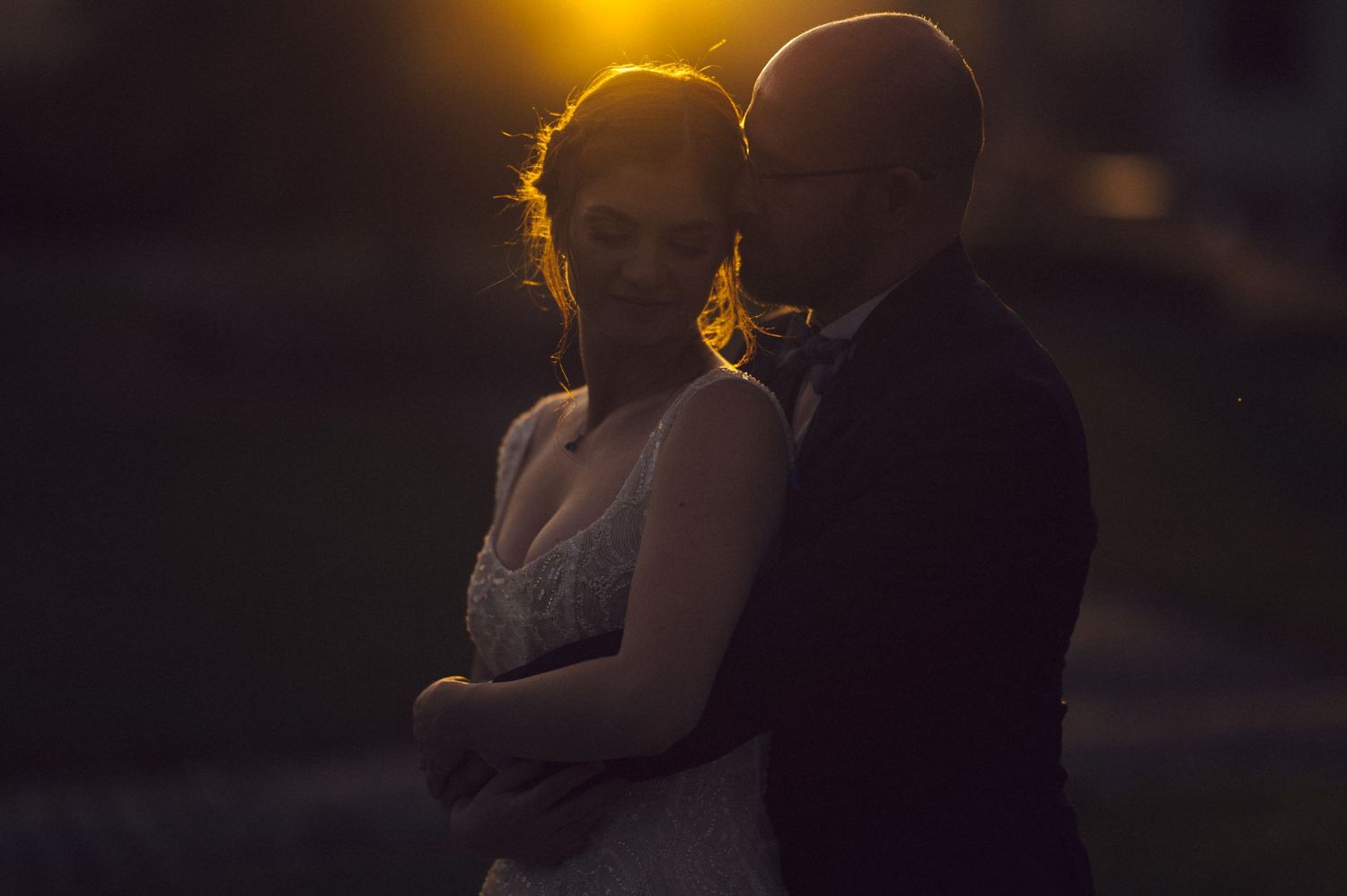 Silhouetted couple in warm sunset lighting share tender moments together during outdoor photoshoot.
