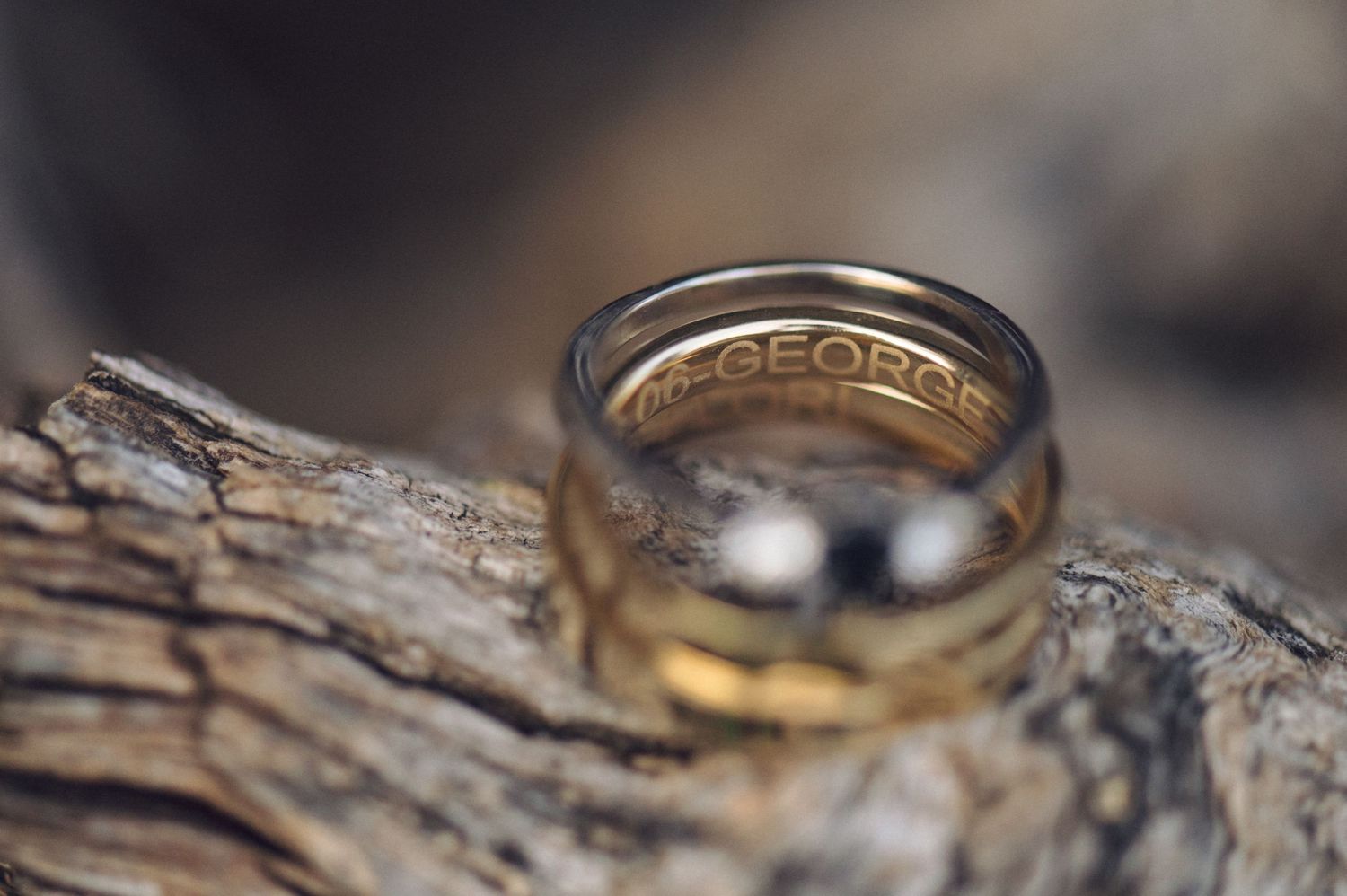Wedding rings with engraved text rest on weathered wood in macro detail.