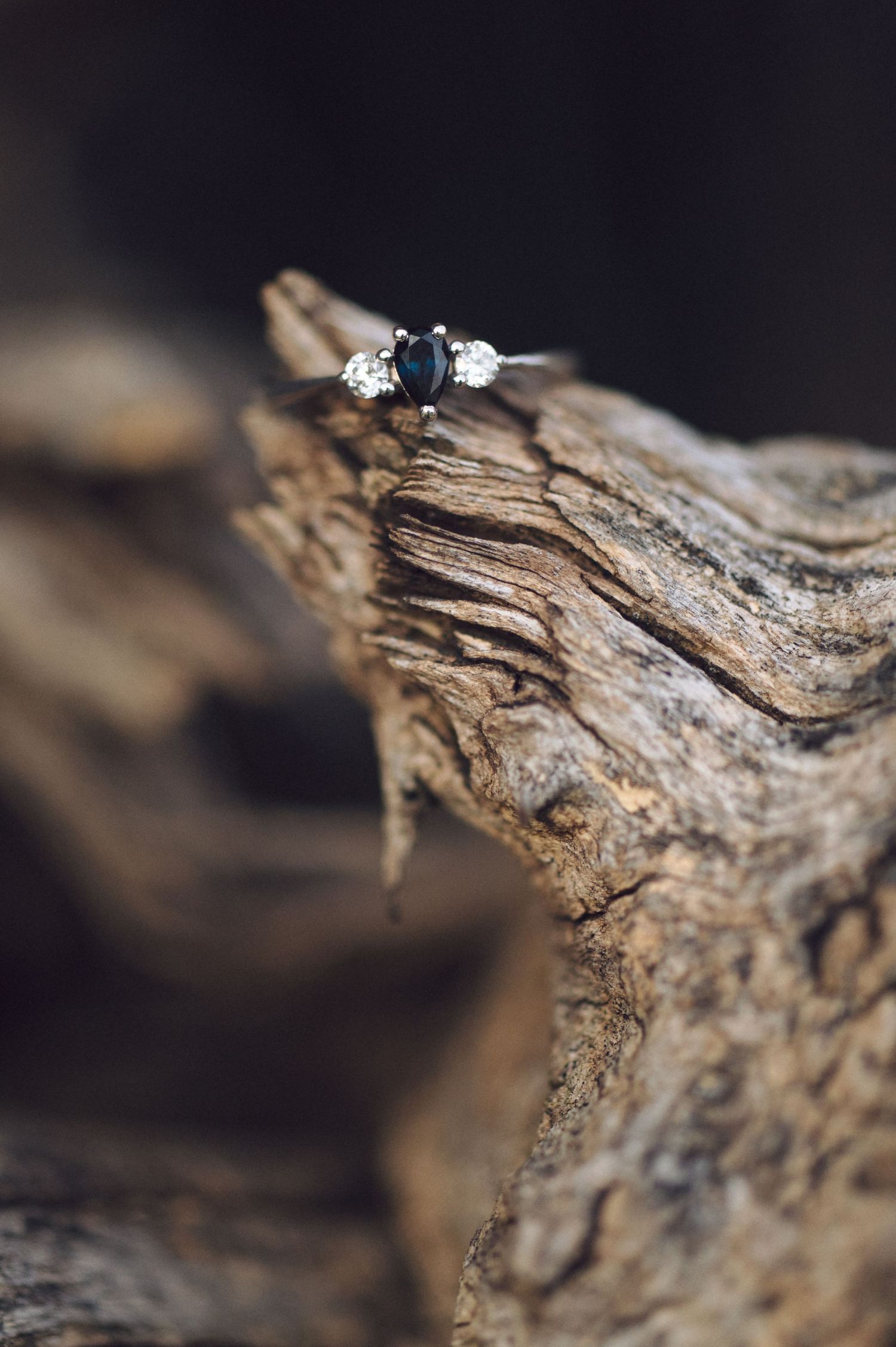 An elegant engagement ring with sapphire and diamonds displayed on textured wood.