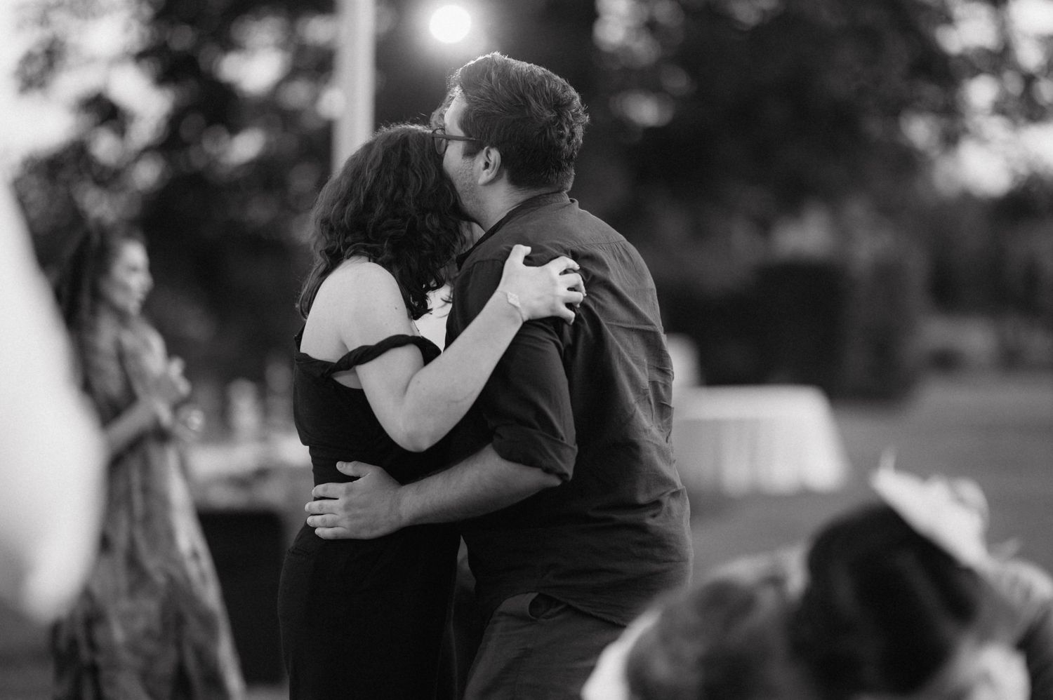 A black and white photo captures an intimate dance embrace between two people at an outdoor gathering.