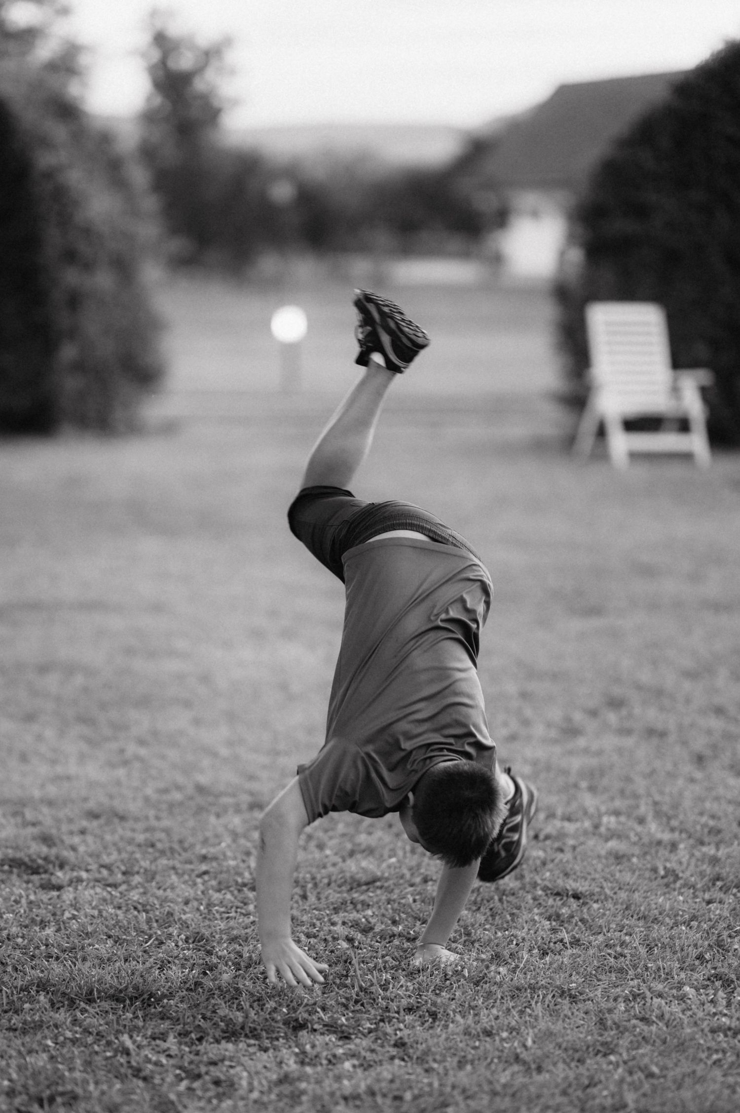 A black and white photo shows someone doing a cartwheel on a grassy lawn at dusk.