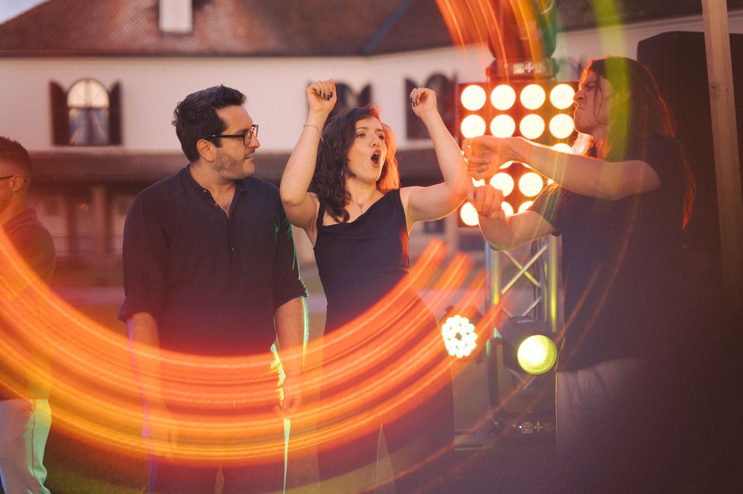 People dancing and celebrating at a party with bright orange lighting effects and stage spotlights in the background.