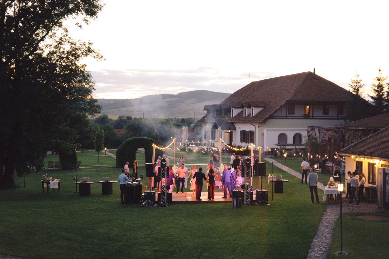 A scenic wedding reception setup with white tents and tables on a grassy hillside at dusk.
