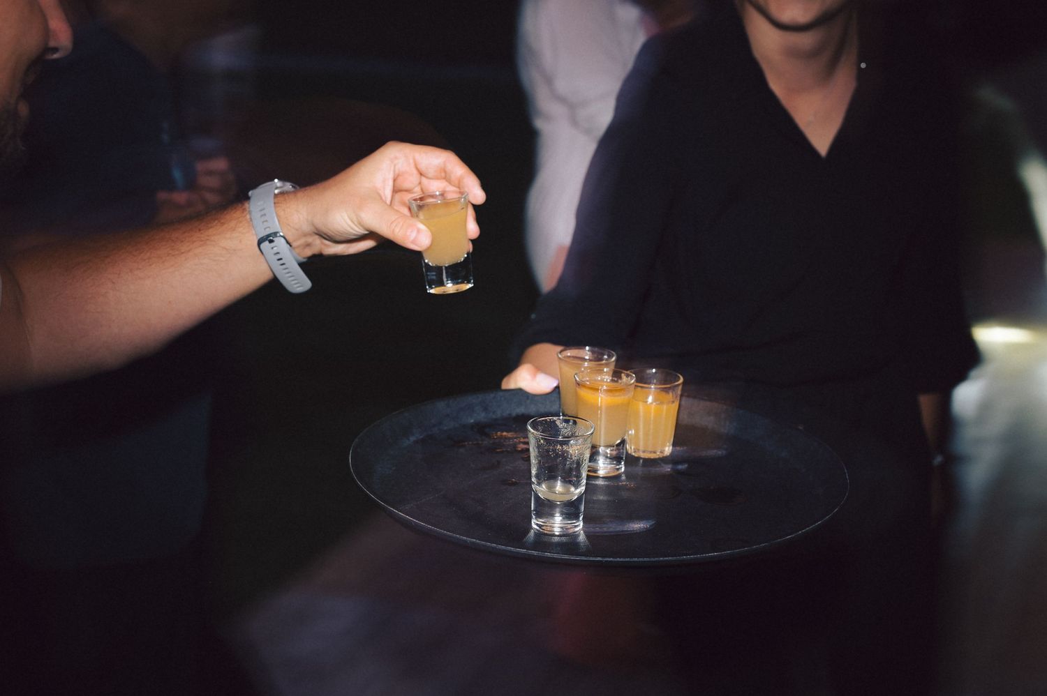 Shot glasses being filled on a serving tray at a dimly lit party setting.