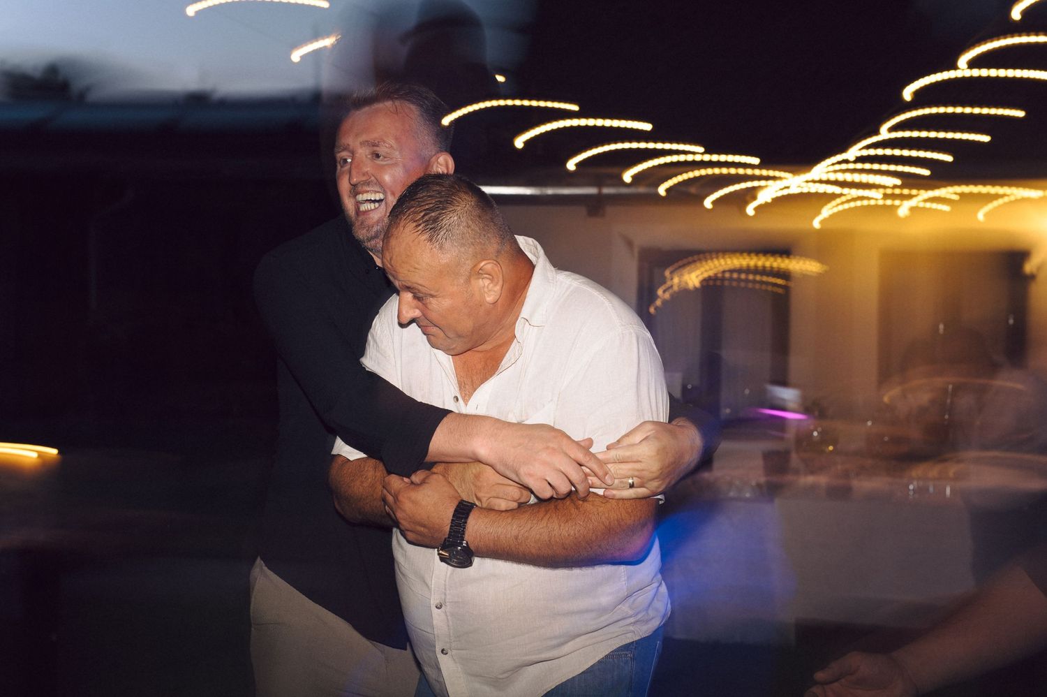 Two people dance together beneath glowing string lights at a nighttime outdoor celebration.