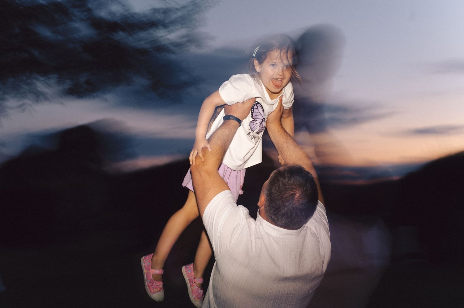 A wedding couple embraces in silhouette against a dramatic sunset sky during their outdoor photoshoot.
