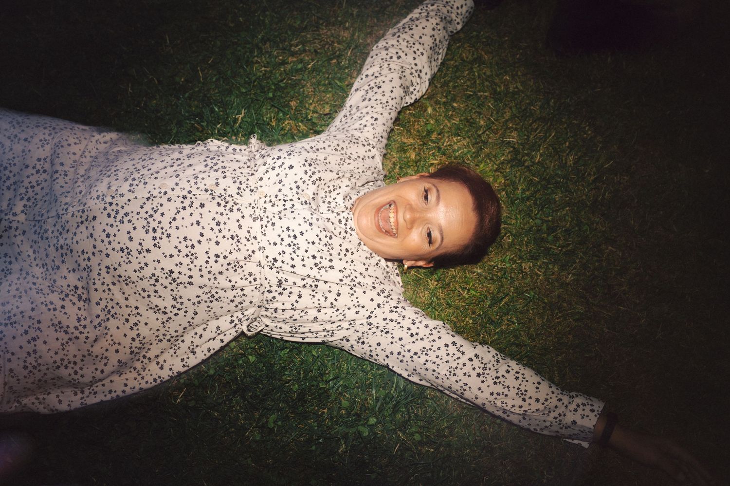 Someone wearing a white patterned sweater lies on green grass in a star-like pose.