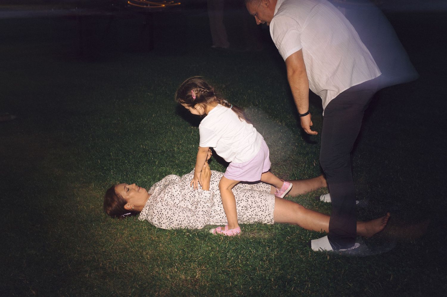 People playing and lying in grass at night with flash photography illuminating the scene.