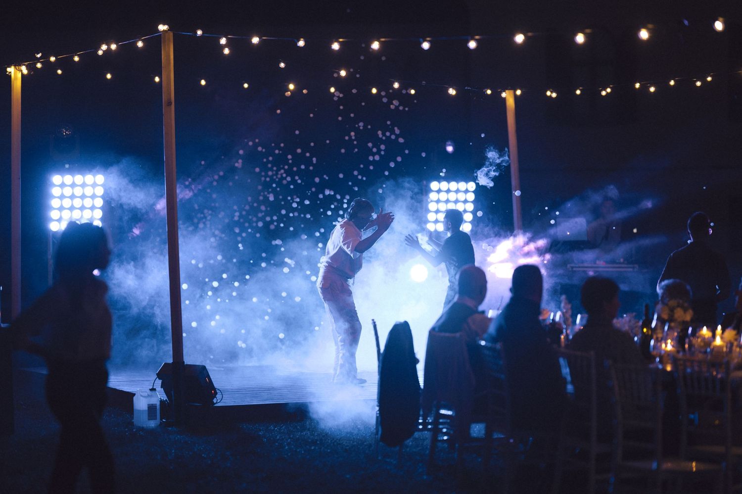 Silhouettes dancing at a nighttime party with string lights and atmospheric fog creating a dreamy ambiance.
