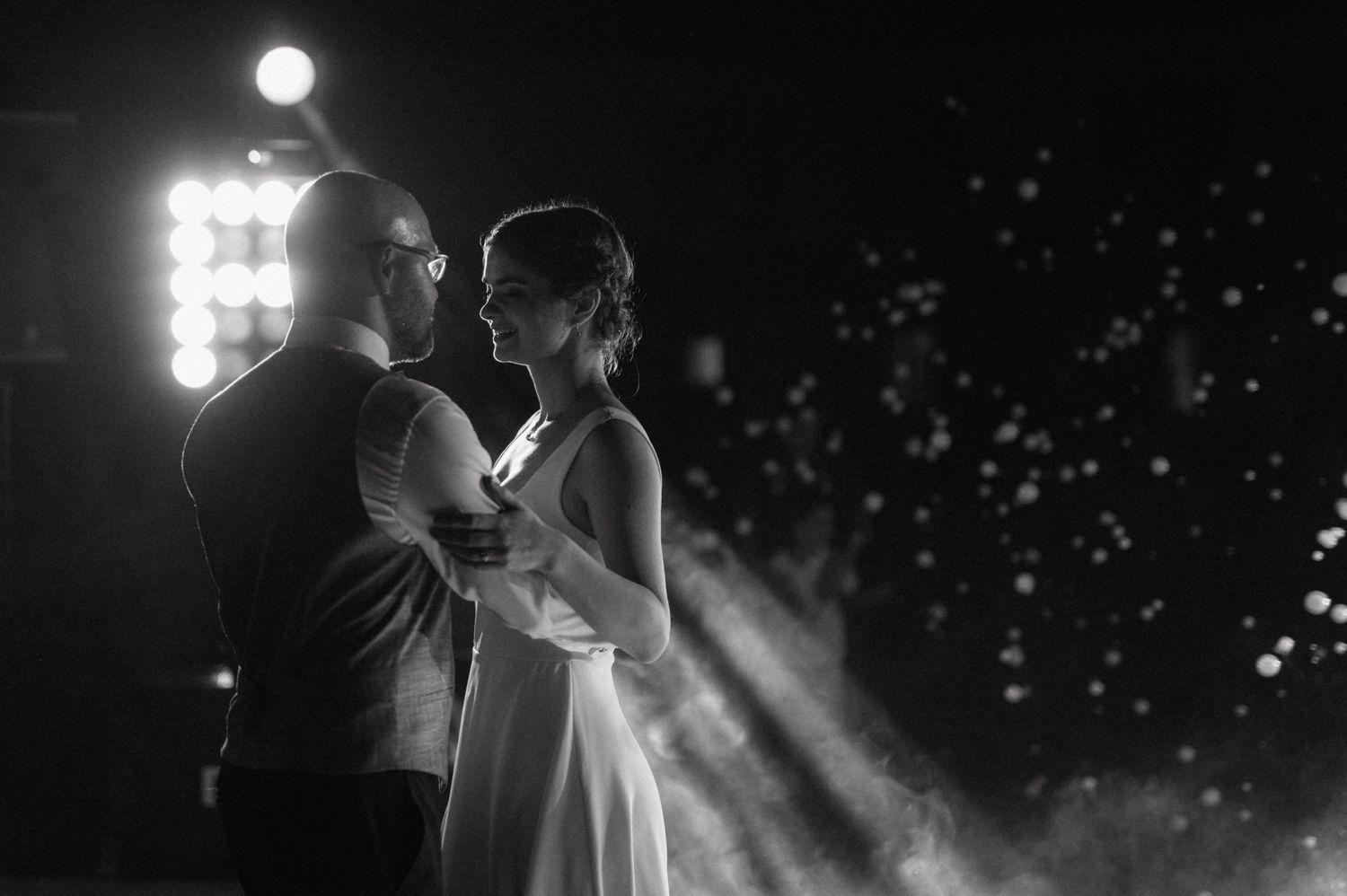 Person in a white wedding dress holding sparklers at night during an outdoor celebration or wedding event.