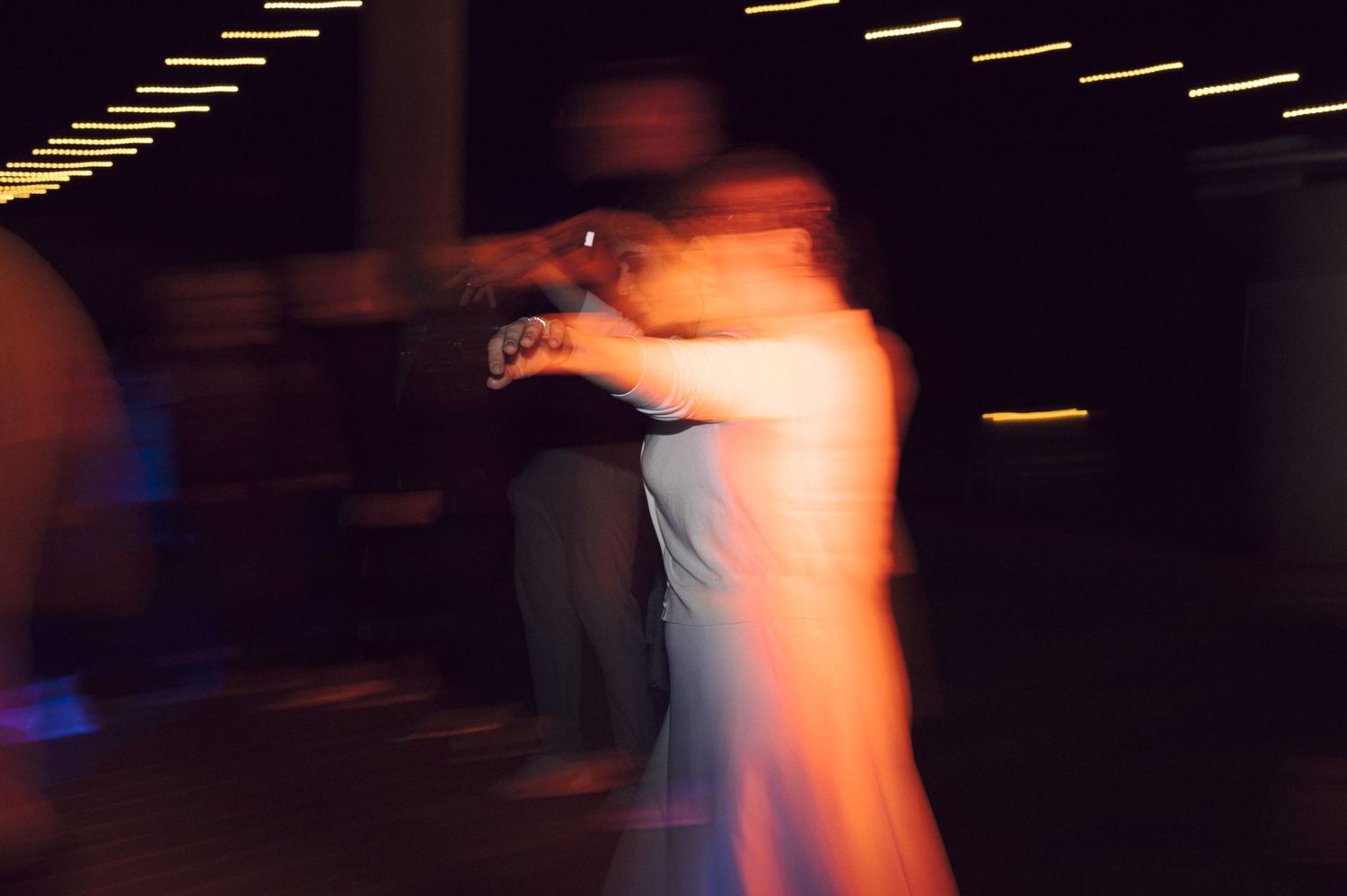 Motion-blurred couple dancing at an event with blue and yellow lighting effects in a dark room.