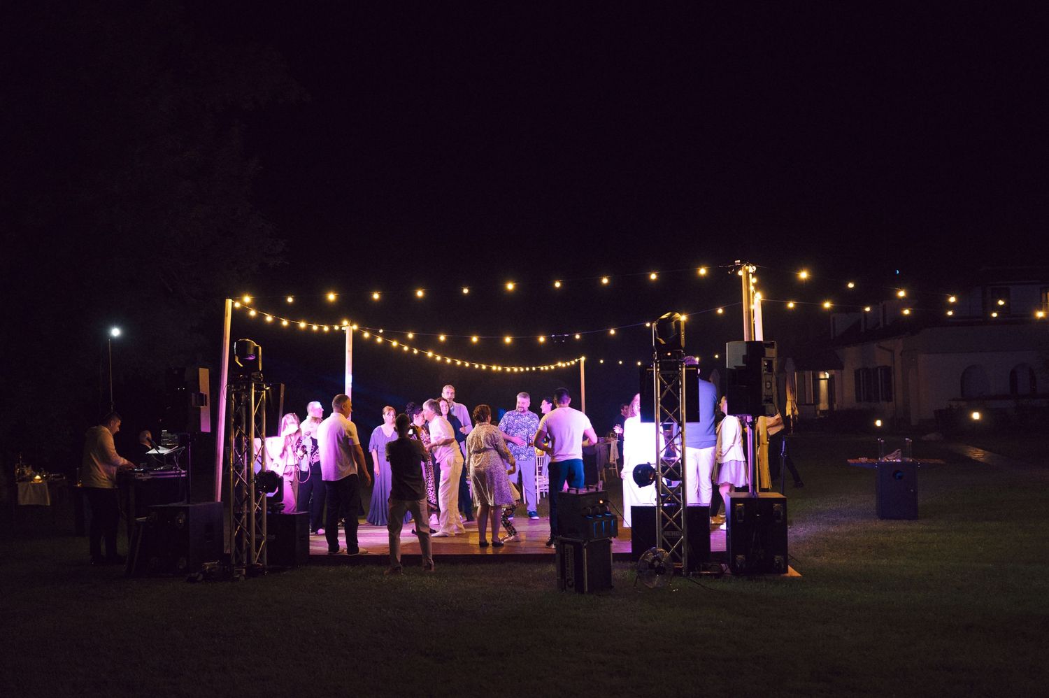 A group of people stand under outdoor string lights during a nighttime gathering.