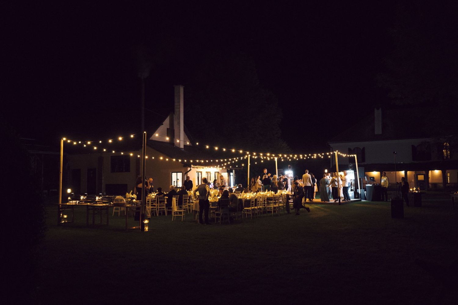 String lights illuminate a nighttime outdoor event with glowing tents and vendor booths against a dark sky.