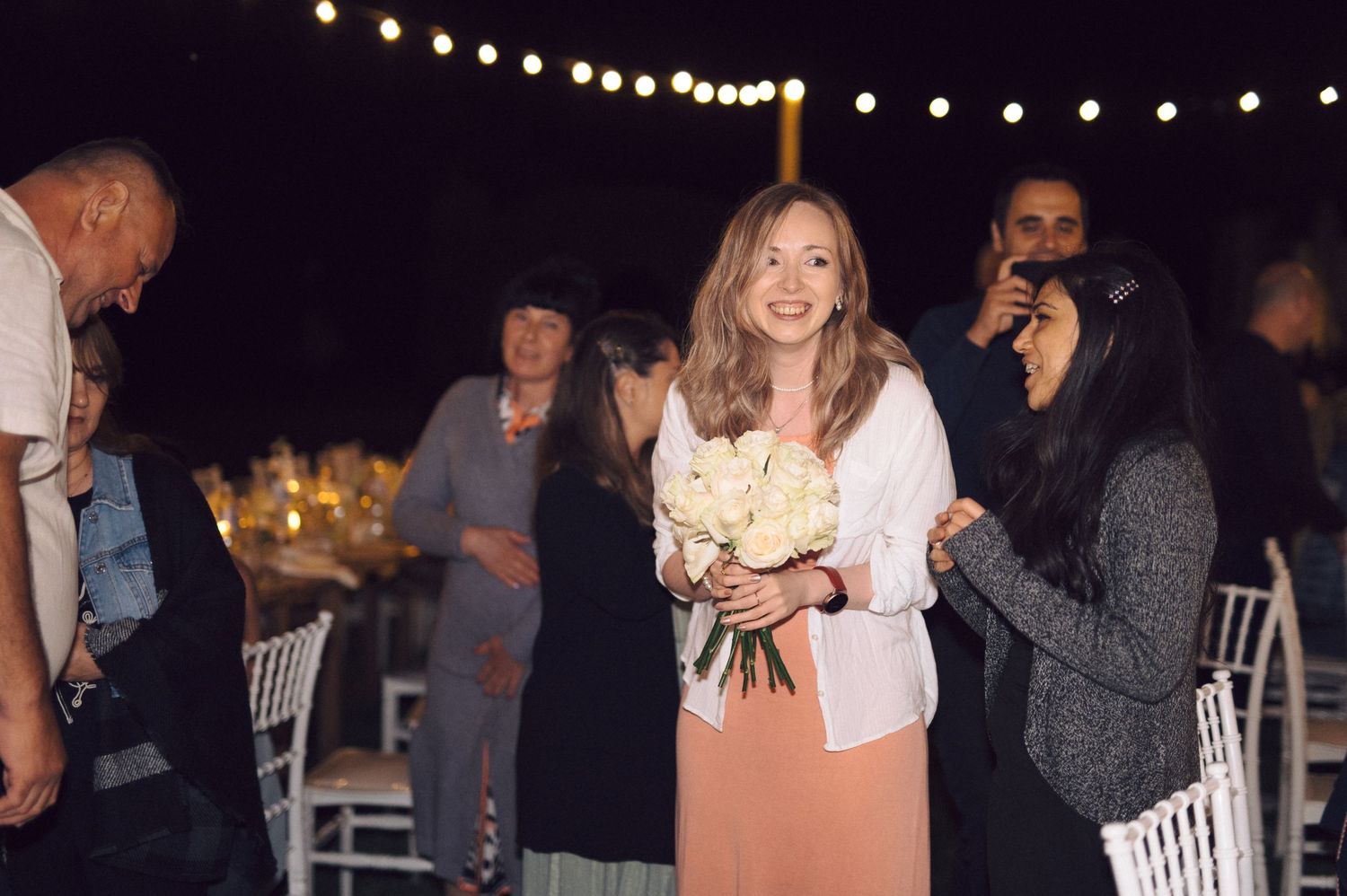 Nighttime celebration with string lights and partygoers dancing under dark sky.