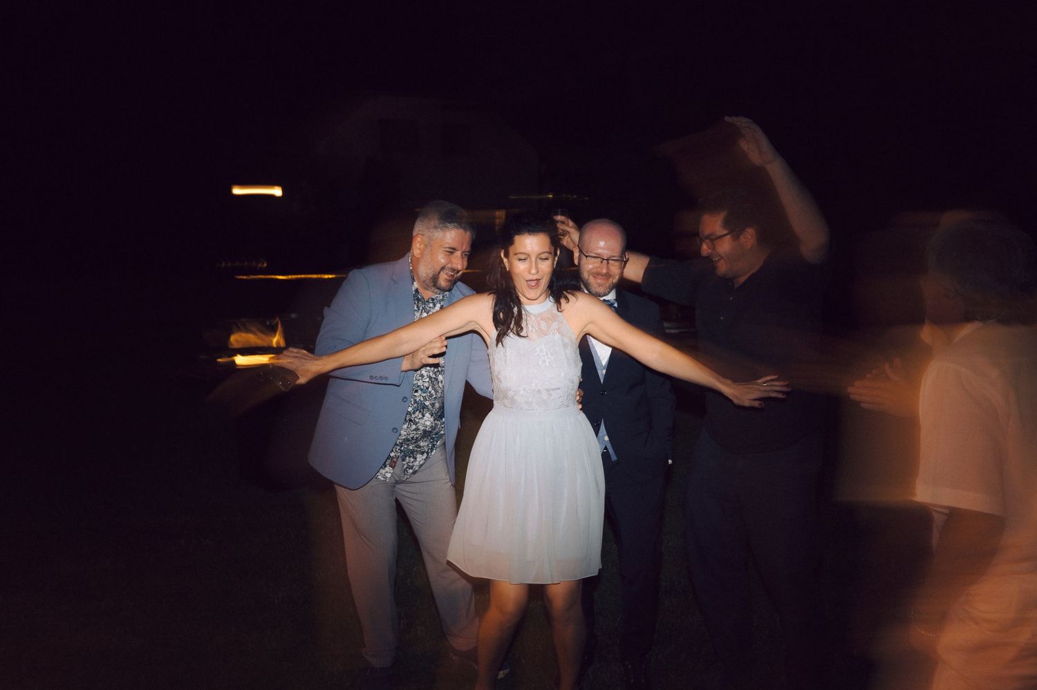 A group dances together under the night sky at an outdoor celebration with soft lighting.