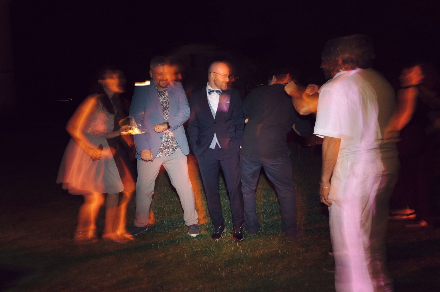 Wedding guests dancing on a dimly lit dance floor at an evening reception celebration.