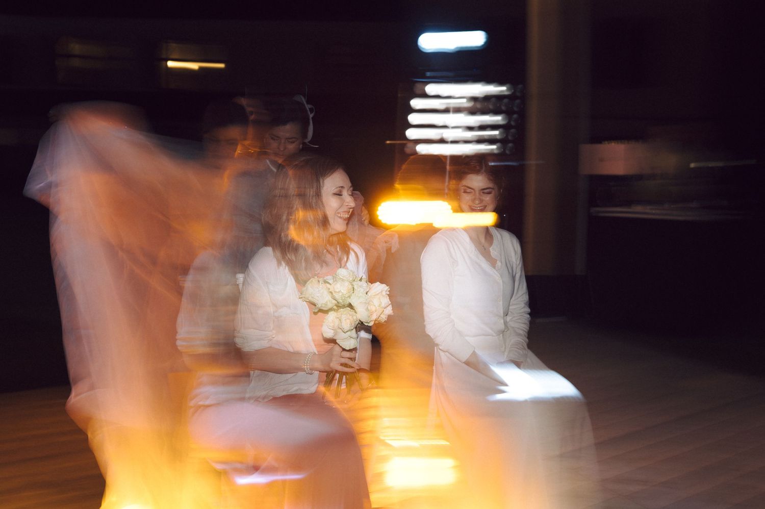 Motion-blurred dancers moving across a dark dance floor illuminated by warm spotlights.