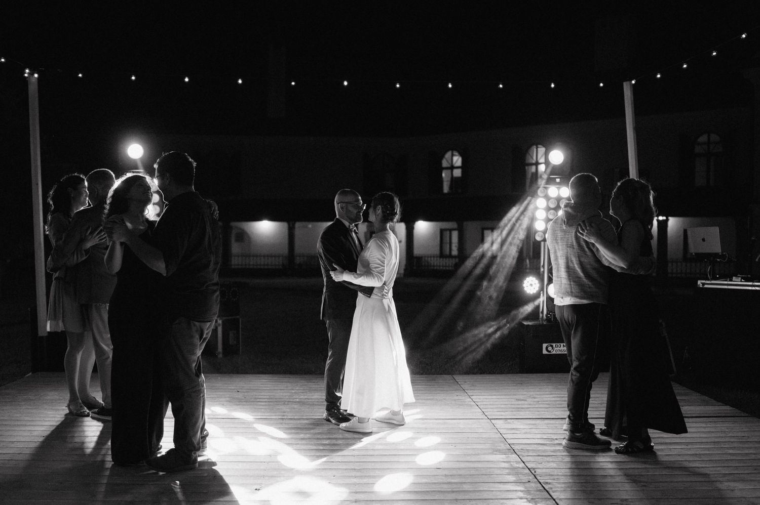 Black and white photo of couples slow dancing on a spotlit dance floor at nighttime.