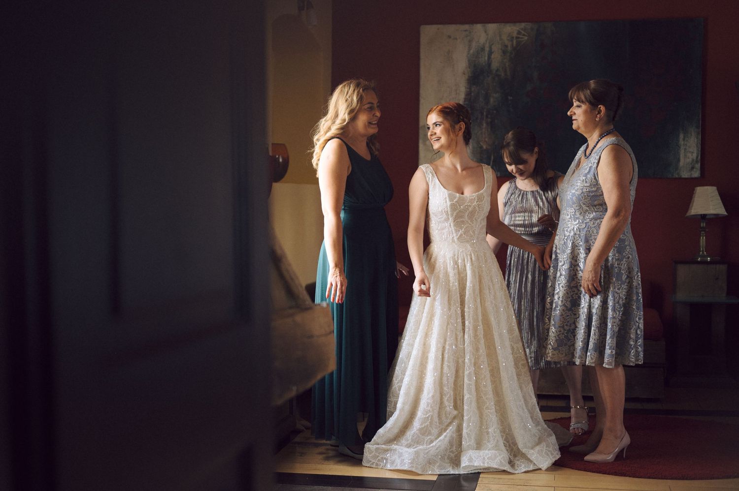 Bridal party with person in elegant white lace wedding gown surrounded by attendants in blue and patterned dresses.