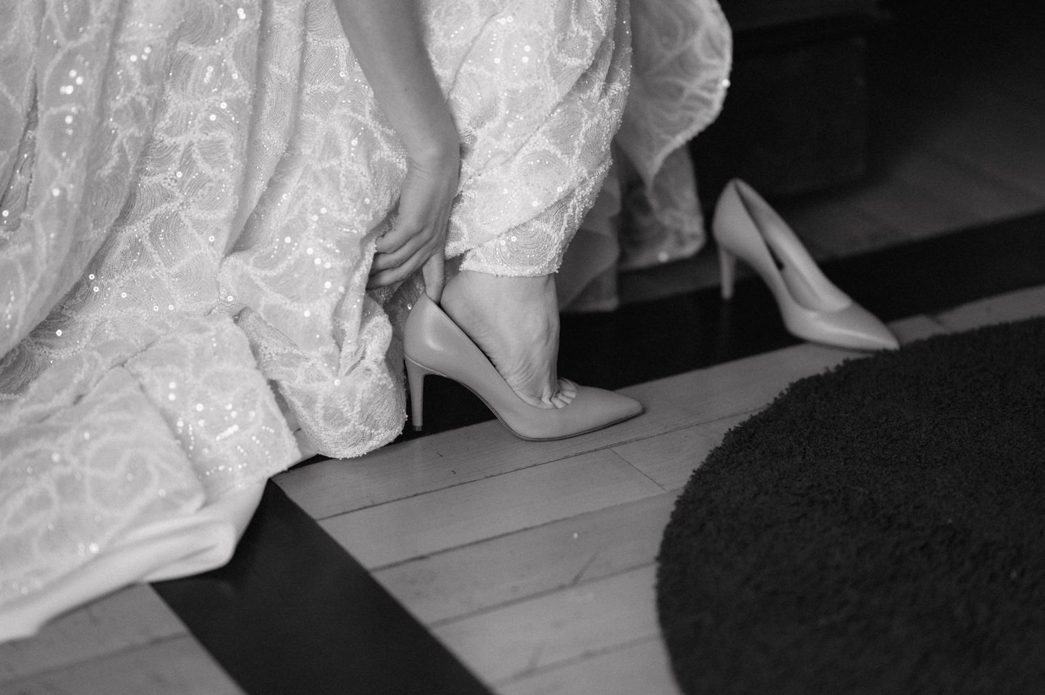 Lace wedding dress train and bottom hem details shown against dark floor with selective focus on fabric texture.