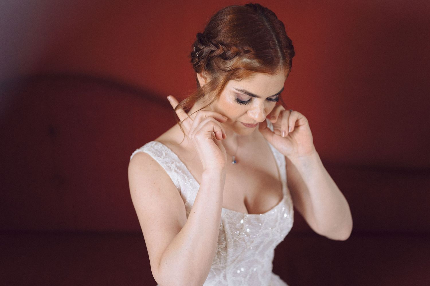 A romantic bridal portrait in a white lace dress against a deep red background with soft lighting and elegant styling.