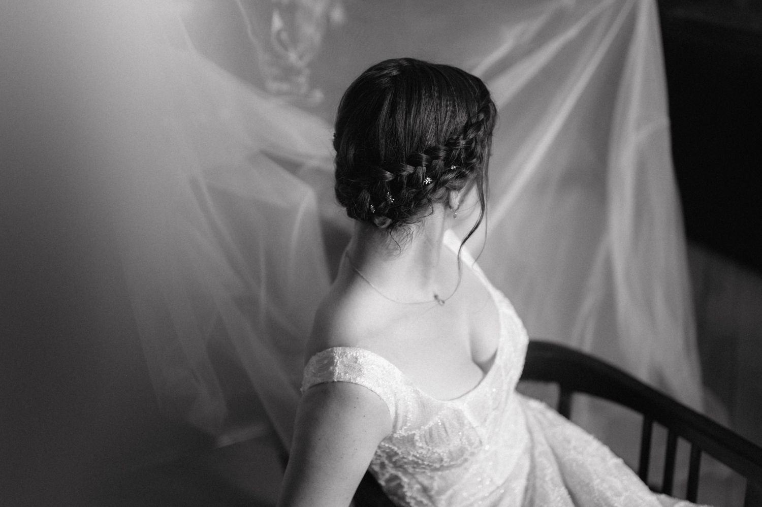 Black and white photograph showing intricate braided hairstyle and lace dress detail against white backdrop.