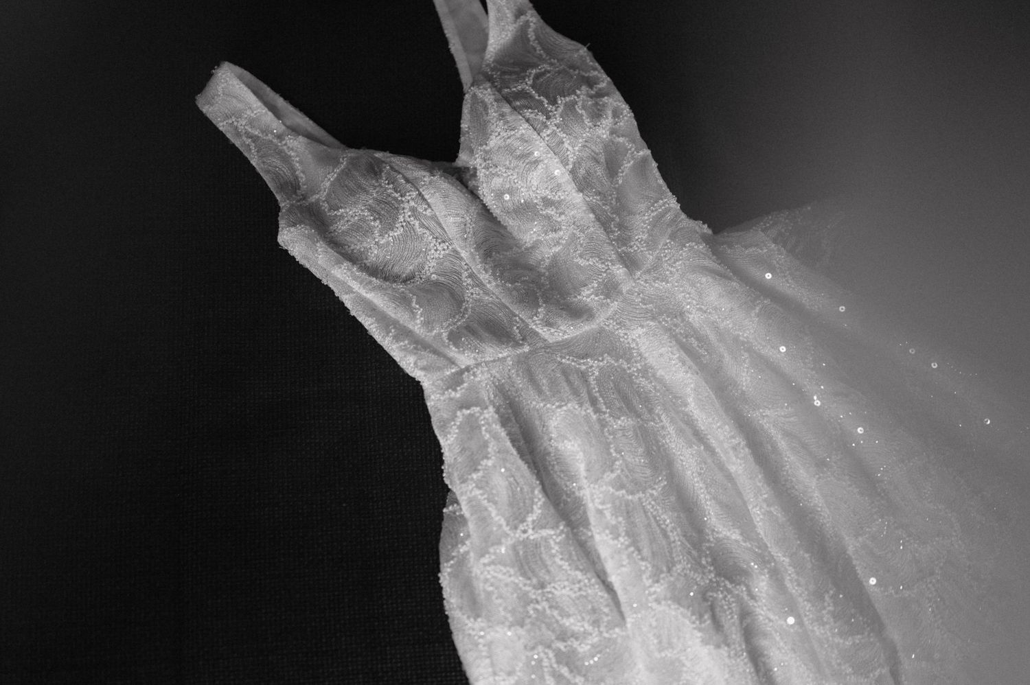 A white sheer organza dress hanging against a dark background with delicate ruffled details and sparkles.