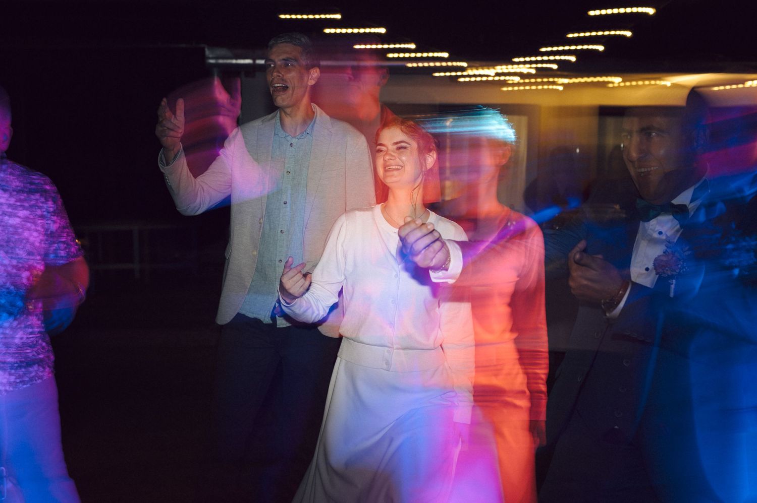 People dancing at a wedding reception with colorful blue and purple lighting effects in a dark venue.