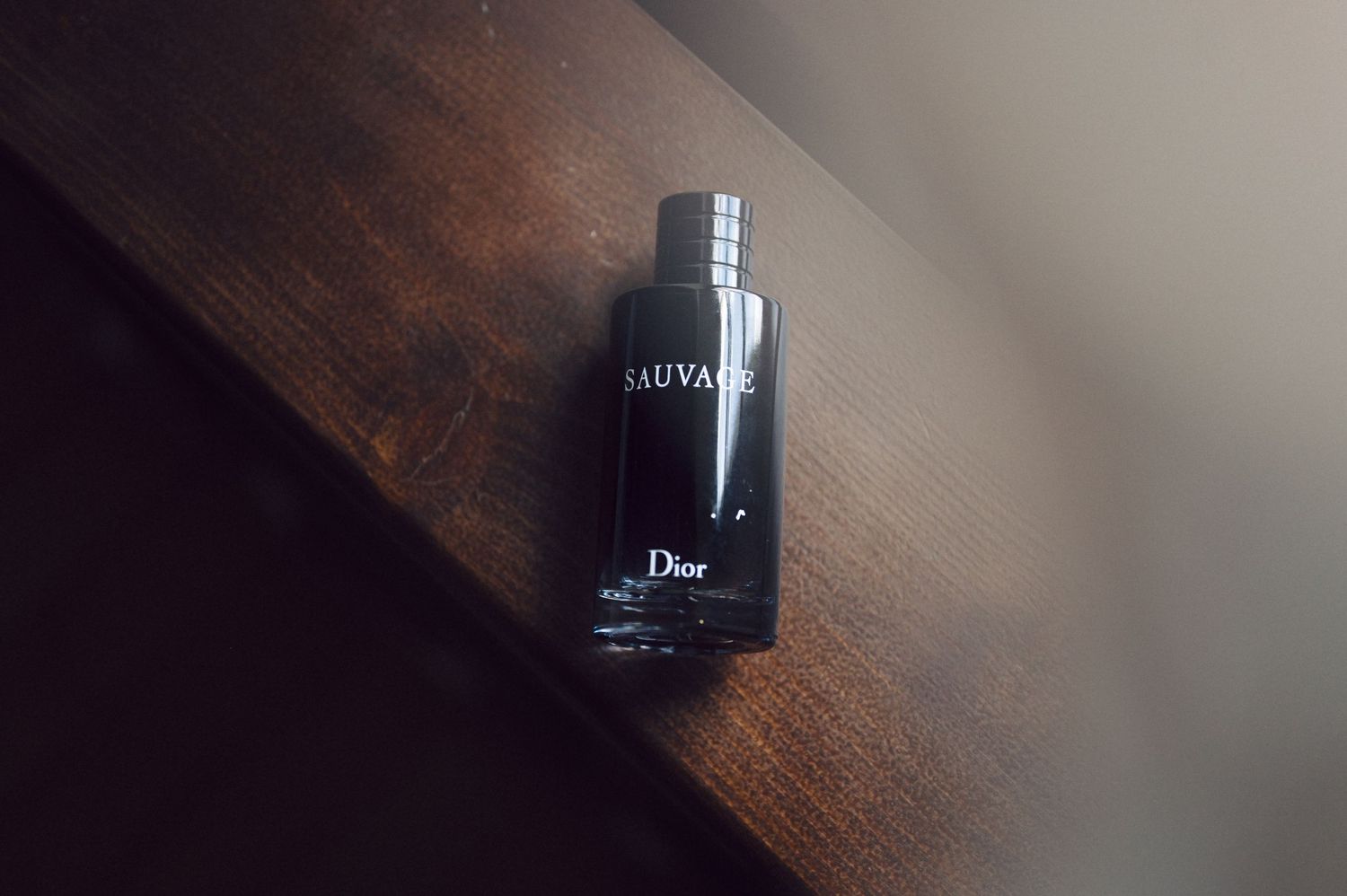 A black Dior Homme fragrance bottle sits on a dark wooden surface in moody lighting.