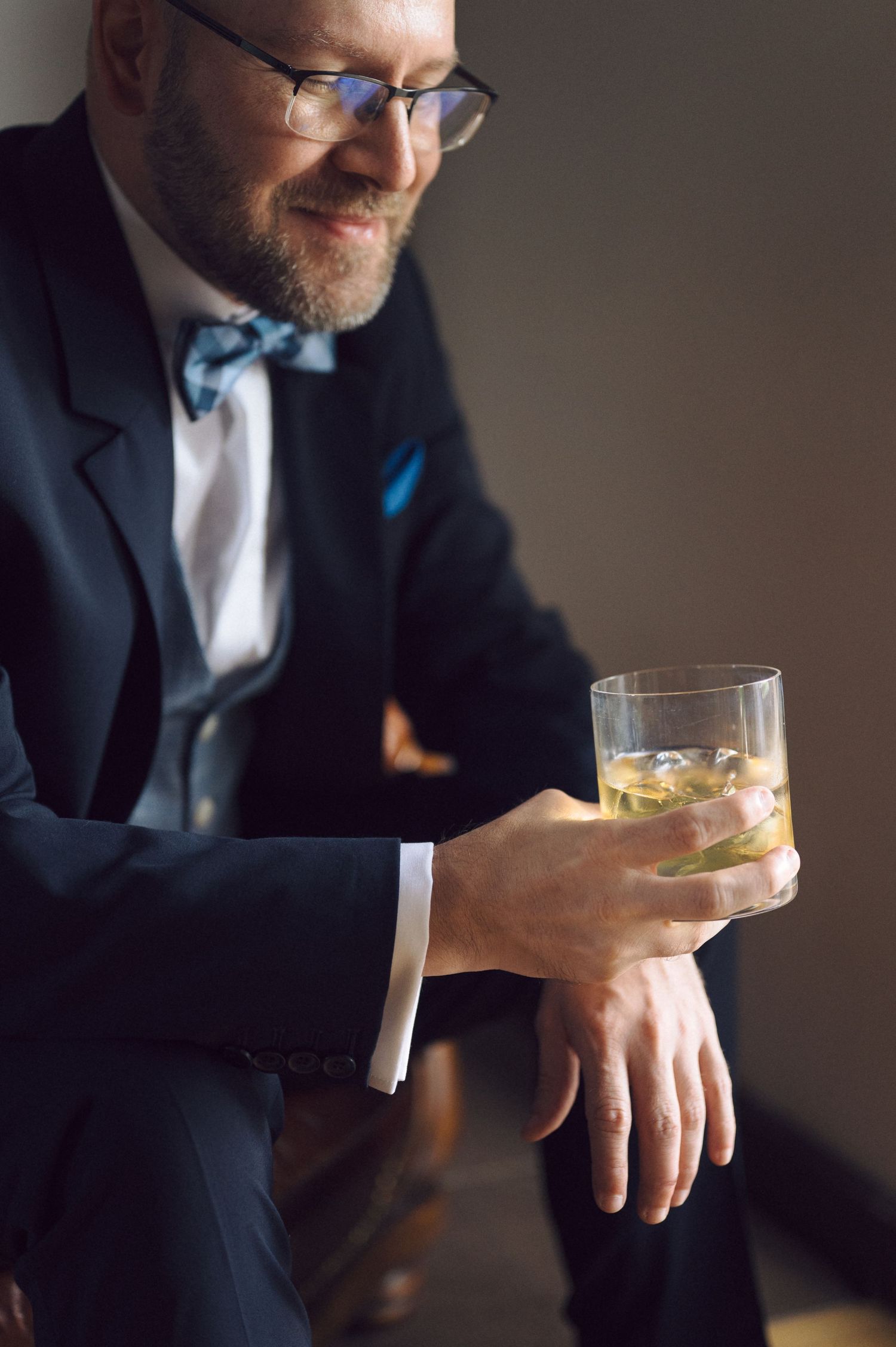 Person in formalwear sits with cocktail glass at dimly lit bar in stylish and moody setting.