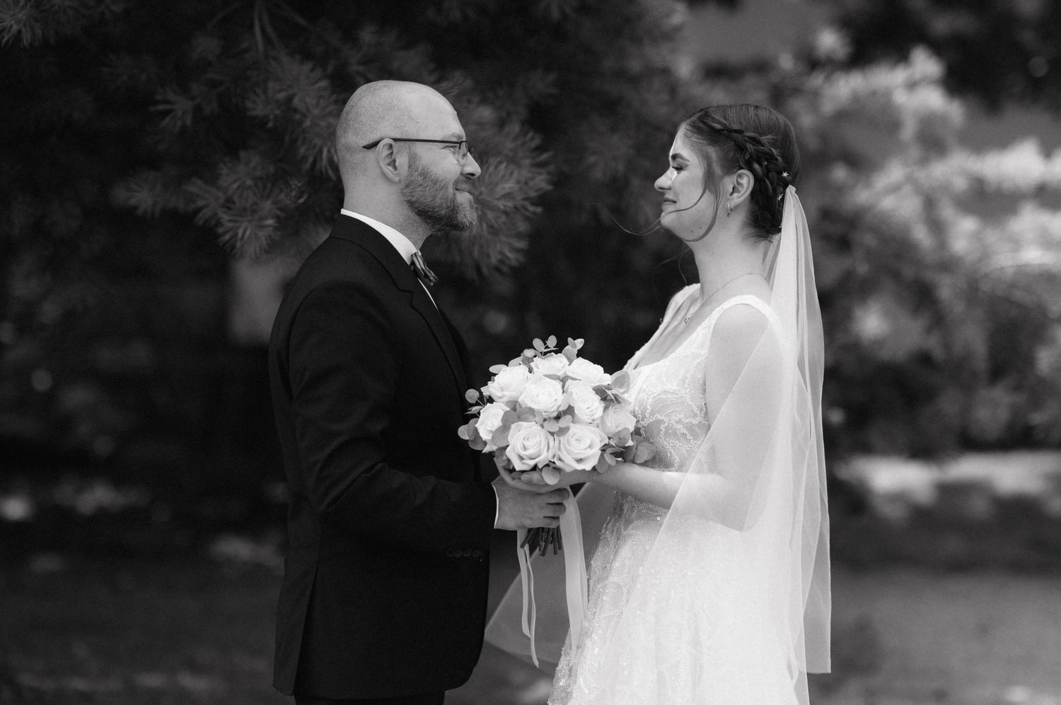 A black and white wedding photograph showing a special moment between a couple holding a bouquet of white flowers.