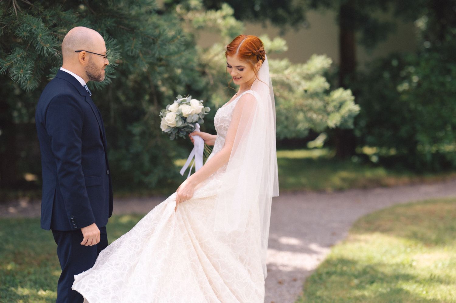 A couple in a park on their wedding day with the bride wearing a flowing white gown with veil and holding a bouquet.