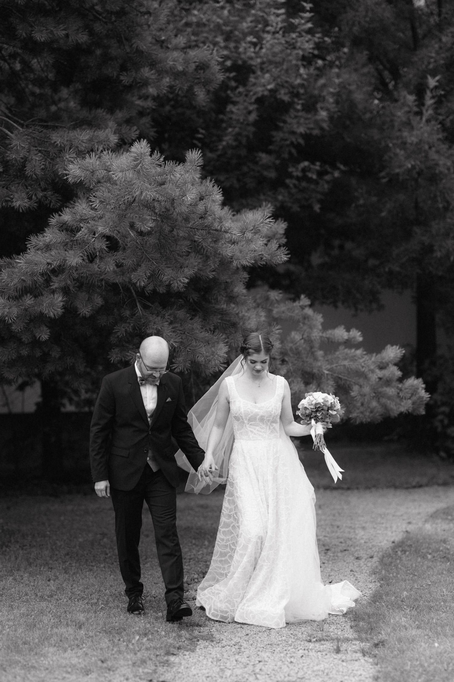 A black and white panoramic sequence of a wedding couple walking through a garden with trees and foliage in the background.