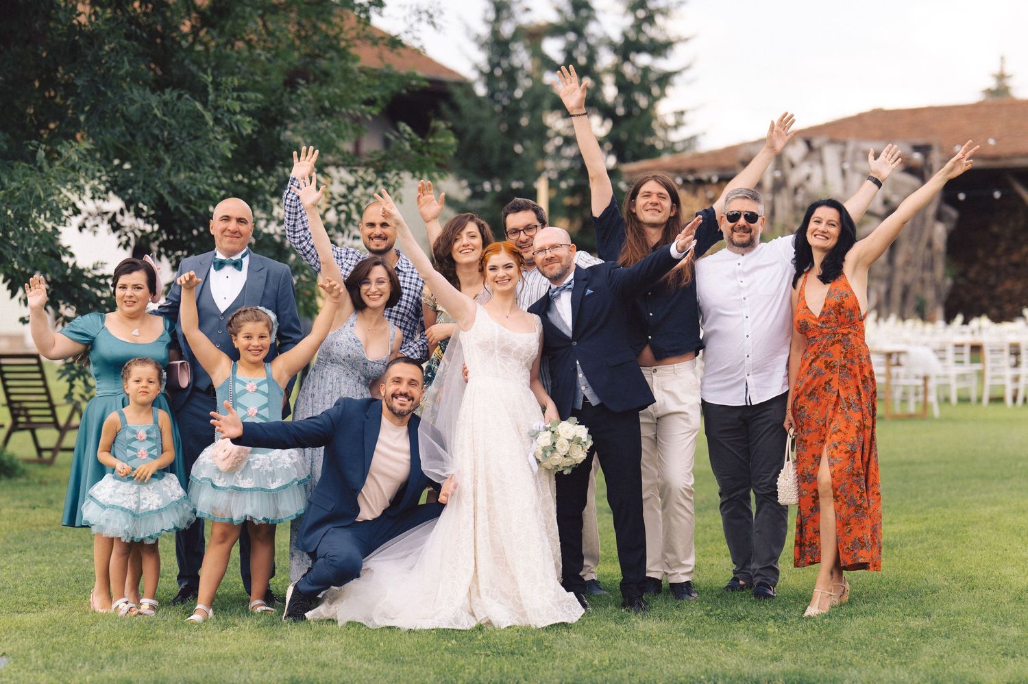 Joyful group jumps together for celebratory photo on grassy lawn during outdoor wedding festivities.