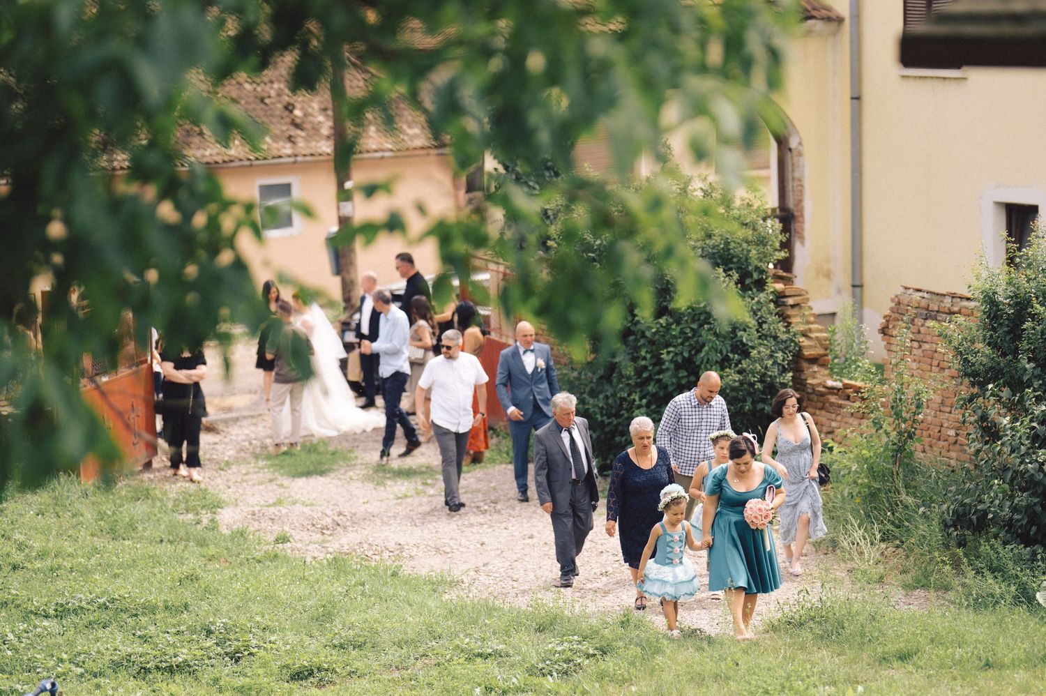 A group of wedding guests walk along a garden path during a daytime celebration on the church grounds.