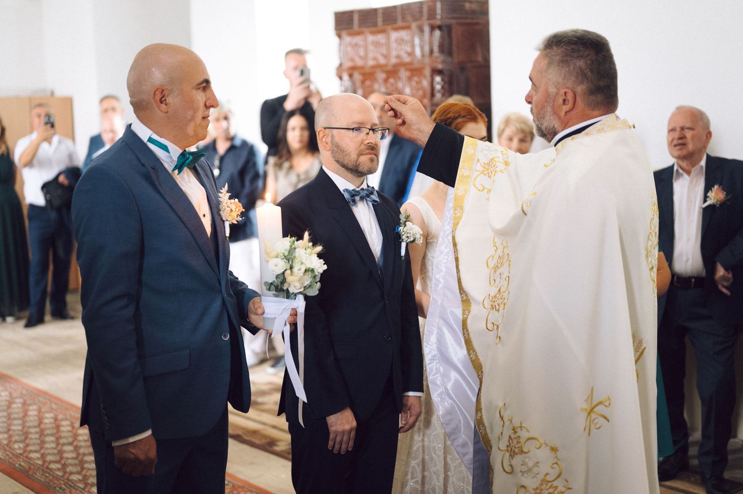 Guests and clergy gathered during a formal indoor wedding ceremony with bride and groom at the altar.