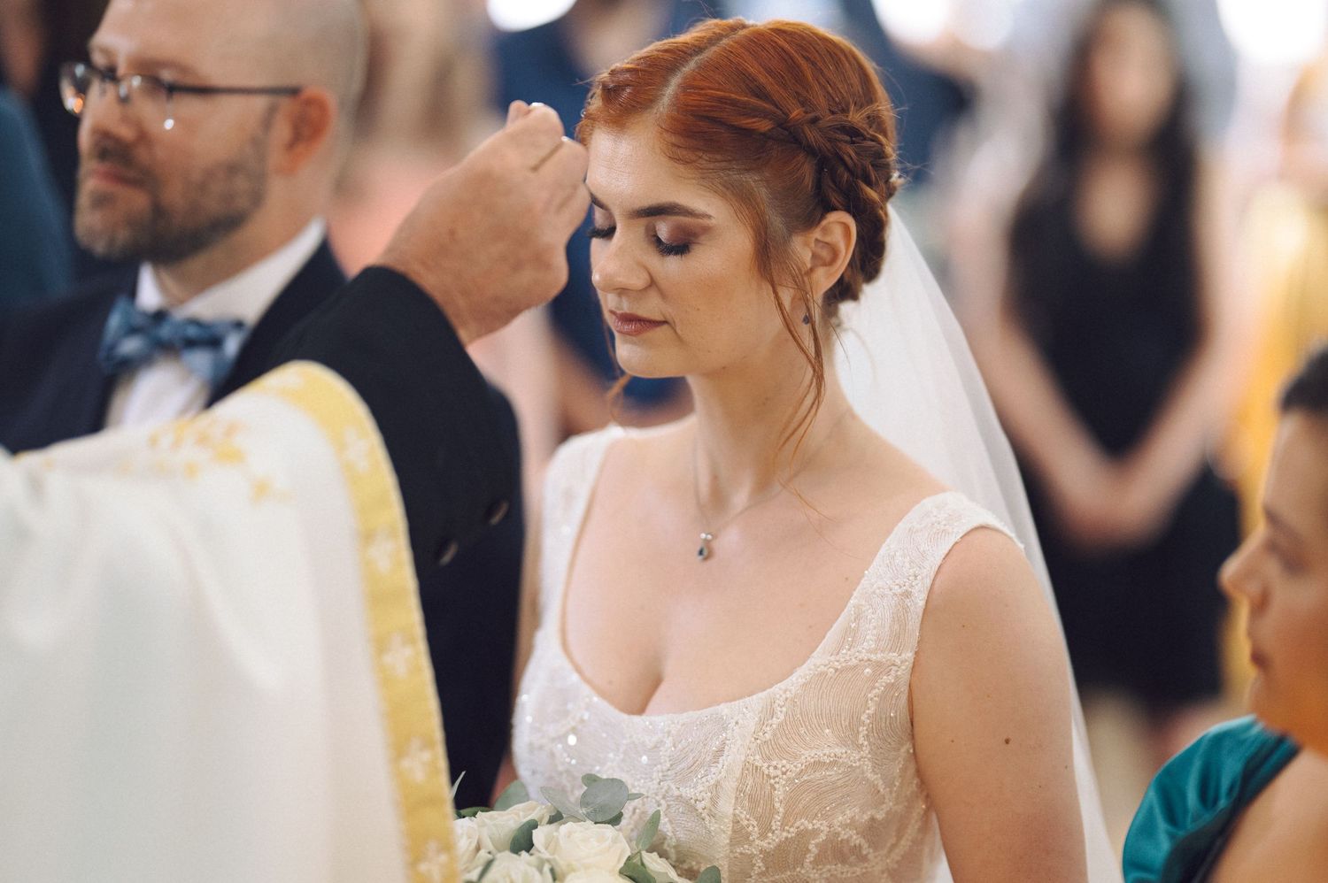 Wedding ceremony attendees in formal attire gathered indoors during a traditional service.