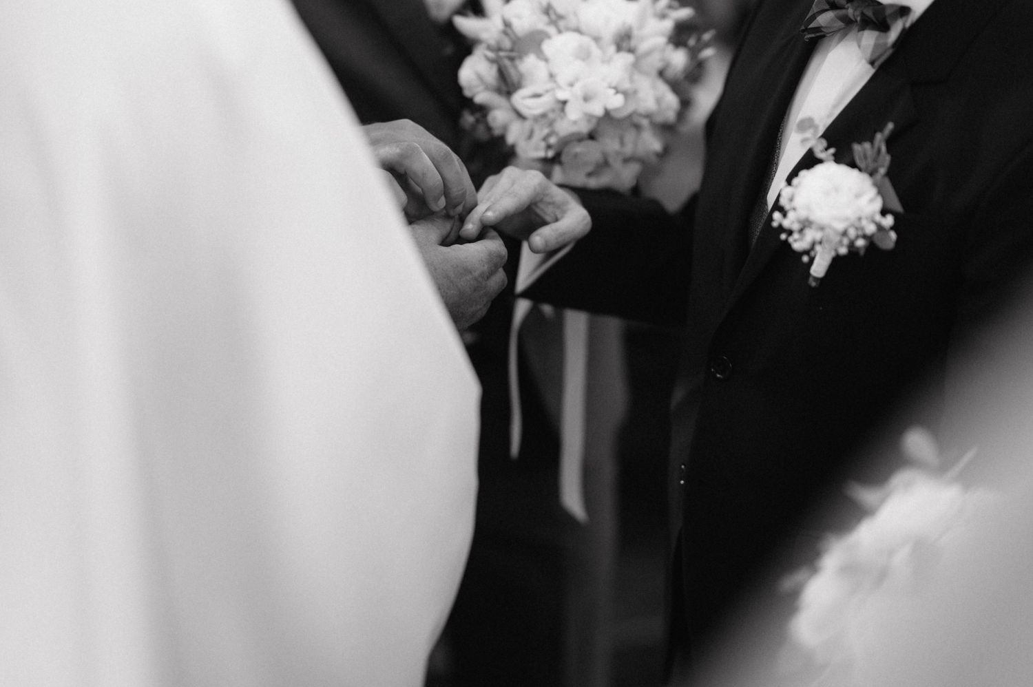 Elegant wedding ceremony moment showing hands exchanging wedding rings against backdrop of white dress details.